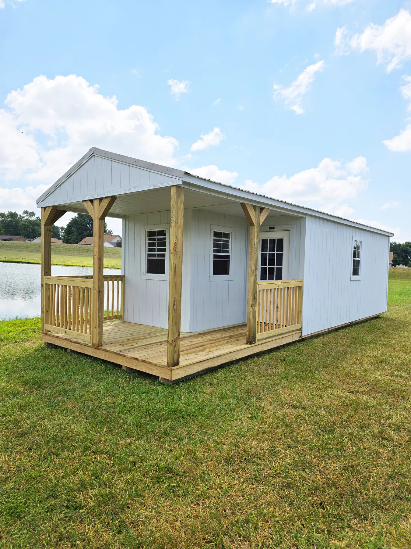 White Premier cabin with a wood porch beside a pond